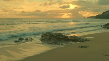 Parlak sarı günbatımında kayalara vuran dalgaların yavaş çekim görüntüsü. Parlak yeşil denizdeki kayalık sahilde dalgalar sarsılıyor. Yeşil deniz dalgalar halinde kayalık sahilde yuvarlanıyor..