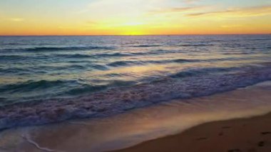 Gökyüzü manzarası denizin üzerinde güzel sarı günbatımı. Döngü videosunda batan güneşin dalgaların üzerindeki gökyüzünü boyadığı, Phuket 'teki kumlu Karon Sahili' nde hafifçe kırdığı güzel bir sahne var..  