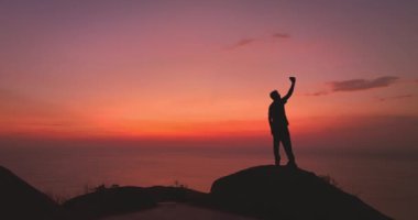 Gün batımında dağın tepesinde sırt çantalı bir adamın silueti.