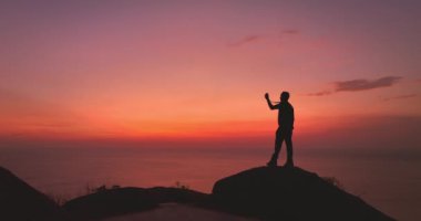 Uçurumun kenarında parlak kırmızı gökyüzünde kırmızı günbatımında bir adam.