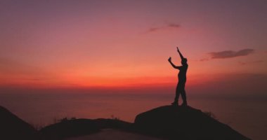 Uçurumun tepesinde, romantik gökyüzünde gün batımında, denizin üstünde bir adam selfie çekiyor.