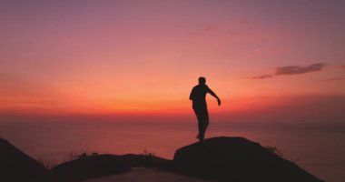 Uçurumda yürüyen ve kızıl gökyüzünde selfie çeken bir adam.