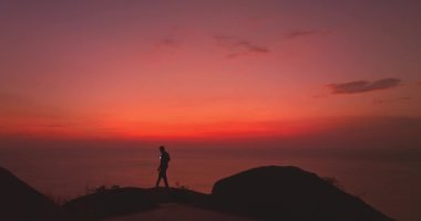 Uçurumda yürüyen ve kızıl gökyüzünde selfie çeken bir adam.