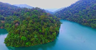 Tayland 'ın güneyindeki Yüzthani ilinin en büyük barajı olan Ratchaprapha Barajı' ndaki adanın yakınındaki yeşil suyun havadan çekilmiş videosu. Arkaplanda yüksek dağlar.