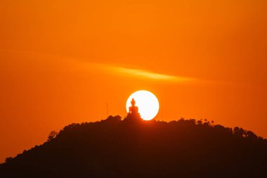 Güneş, Büyük Buda 'nın arkasındaki kırmızı gökyüzünde dönüyor. Kızıl gökyüzünde güneşin etrafında dönen muhteşem Phuket Büyük Buda heykeli. Heykelin güzelliği büyüleyici doğaya mükemmel uyuyor. kırmızı gökyüzü arkaplanı