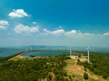 Lam Takong Barajı, Nakhon Ratchasima, Tayland 'daki dağın tepesindeki rüzgar türbinlerinin üstündeki mavi gökyüzündeki beyaz bulutların hava görüntüsü. Rüzgar enerjisi elektrik üretir. Temiz enerji.