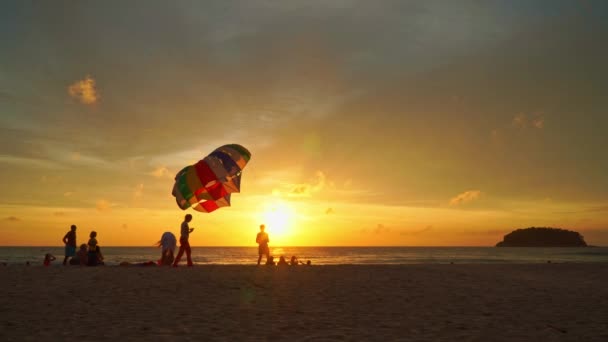 プーケット 2023 観光客はカタビーチでリラックスします プーケット 観光客は 黄金の太陽の下でビーチで写真を撮ります 美しい夕日のカラフルなパラセーリング — ストック動画