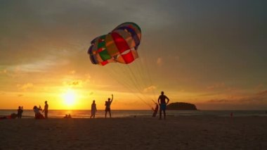 .Phuket, Tayland-12 Ağustos 2023: turistler Kata plajında rahatlar Phuket... turistler altın güneşin altında fotoğraf çekerler... güzel gün batımında renkli deniz paraşütü... parlak altın gökyüzü arka planı.