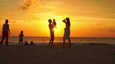 .Phuket, Tayland-12 Ağustos 2023: turistler Kata plajında rahatlar Phuket... turistler altın güneşin altında fotoğraf çekerler... güzel gün batımında renkli deniz paraşütü... parlak altın gökyüzü arka planı.