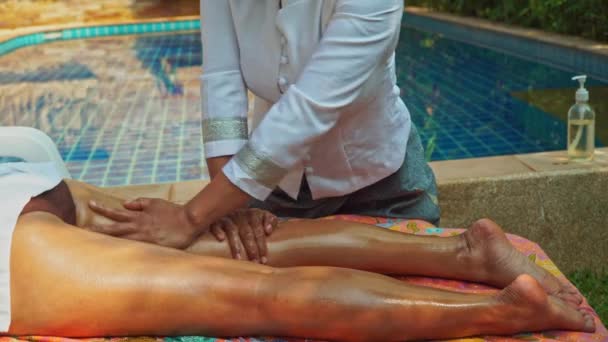 女性はマッサージ師がマッサージオイルで彼女の体をマッサージするようにプールによって快適に横たわります — ストック動画