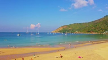 .Nai Harn plajında yeşil denizin üzerindeki güzel mavi gökyüzü. - Nai Harn Körfezi 'nde demirlemiş turistik tekne ve yatlar. - Turist kalabalığı sahilde dinleniyor. .deniz dalgaları kıyı zeminine çarpıyor.