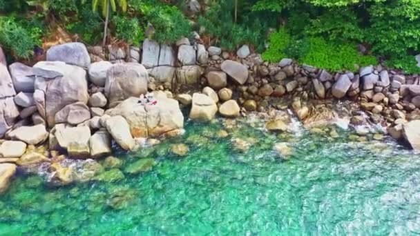 鸟瞰绿松石海旁边的岩石和山脚的绿林岛上周围的岩石与绿松石海的对比平静的海浪冲击着普吉岛的岩石岩石质感背景 — 图库视频影像