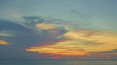 Güzel günbatımının süratine denizin üzerinde, eğimli gökyüzünde yumuşak bulutlar eşlik eder.