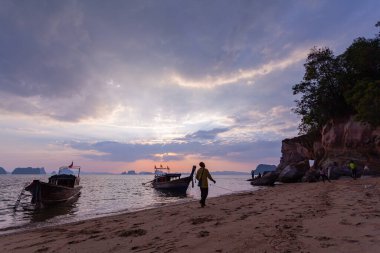 .Uzun kuyruklu tekneler turistlerin tuhaf şekilli pelerini ziyaret etmelerini bekliyor pelerin pembe renkte ve tatlı günbatımında büyük bir oyuk okyanusun üzerinde büyüleyici pembe bir günbatımı..