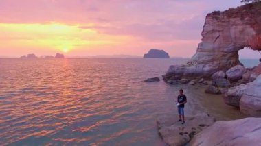 Renkli mağaranın altındaki büyük bir deliğin önünde dron uçuran bir adam. Pelerin pembe, gün batımında kocaman bir oyuk var..
