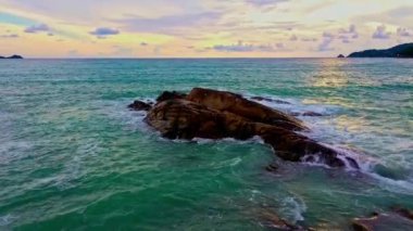 Patong sahilindeki dalgaların hava manzarası. Parlak yeşil denizdeki kayalık sahilde dalgalar sarsılıyor. 