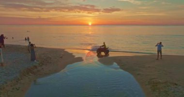 Kumsaldaki dolambaçlı kanalın hava görüntüsü. Turistler kumlu bir sahildeki küçük bir kanalın yanında batan güneşi seyrediyorlar. Kanaldaki güzel gökyüzü yansıması..