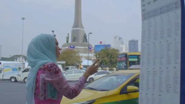 かわいいイスラムの女性がバンコクの中心部のバスラインを探しています 青いヘッドスカーフを身に着けているかわいいイスラムの女性 重い交通背景 — ストック動画