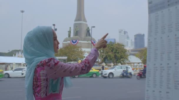 かわいいイスラムの女性がバンコクの中心部のバスラインを探しています 青いヘッドスカーフを身に着けているかわいいイスラムの女性 重い交通背景 — ストック動画