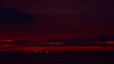 Alacakaranlıkta inanılmaz kırmızı bir gökyüzü. Denizdeki bir yolcu gemisi turistleri sudaki günbatımını seyretmeye götürüyor. Bir yolcu gemisinde mutluluk ve eğlence..