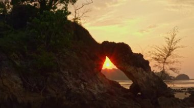 Alışılmadık kaya dalgasının deliğinde güzel bir gün batımı, Ranong Tayland 'daki Phayam Adası' ndaki Hin Talu Buffalo plajında orta atmosferde bir deliği olan kemer gibi oyuğa aşındı..