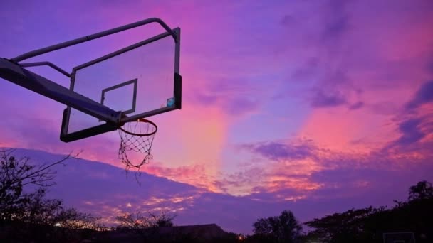 アスリートはボールをバスケットボールフープに撮影しようとします 日没の背景にある景色の日没の空 スローモーション — ストック動画