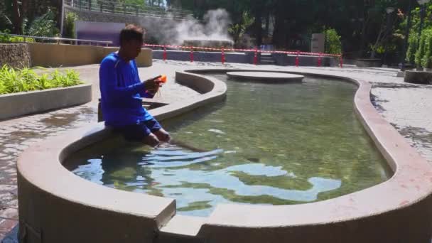 一名男子在温泉浴场坐在温泉池的座位上 坐在温泉池中观看手机 游客们把脚浸在温泉池里放松一下 — 图库视频影像