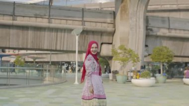 Güzel bir Müslüman kadın Bangkok 'un göbeğinde seyahat ederken gökyüzü treniyle fotoğraf çektirmek için mutlu bir şekilde poz veriyor. - Hareketli şehirde kamera onu çekerken kendine güvenerek gülümsüyor. uygarlık şehri.