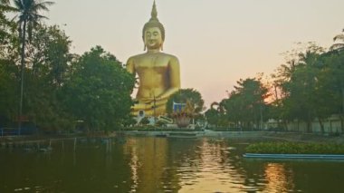 Gün batımında sarı gökyüzü en büyük Buda 'nın arkasında. Havuzda sarı gökyüzünün yansıması. Wat Muang Ang Thong Tayland 'da altın büyüklüğünde Buda' nın meşhur simgesi..