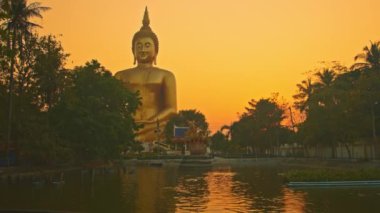 Gün batımında sarı gökyüzü en büyük Buda 'nın arkasında. Havuzda sarı gökyüzünün yansıması. Wat Muang Ang Thong Tayland 'da altın büyüklüğünde Buda' nın meşhur simgesi..
