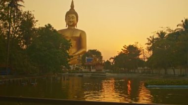 Gün batımında sarı gökyüzü en büyük Buda 'nın arkasında. Havuzda sarı gökyüzünün yansıması. Wat Muang Ang Thong Tayland 'da altın büyüklüğünde Buda' nın meşhur simgesi..