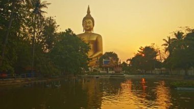Gün batımında sarı gökyüzü en büyük Buda 'nın arkasında. Havuzda sarı gökyüzünün yansıması. Wat Muang Ang Thong Tayland 'da altın büyüklüğünde Buda' nın meşhur simgesi..