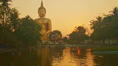 Gün batımında sarı gökyüzü en büyük Buda 'nın arkasında. Havuzda sarı gökyüzünün yansıması. Wat Muang Ang Thong Tayland 'da altın büyüklüğünde Buda' nın meşhur simgesi..