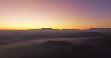 Hava manzarası, sabah güneşinin sisli denizin üzerindeki altın ışığı. Vadide sakin bir akşam atmosferi oluşur. Dağ sırasının renkli renkleri.