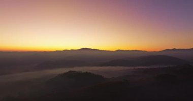 Hava manzarası, sabah güneşinin sisli denizin üzerindeki altın ışığı. Vadide sakin bir akşam atmosferi oluşur. Dağ sırasının renkli renkleri.
