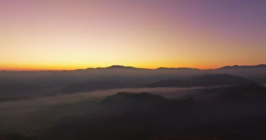 Hava manzarası, sabah güneşinin sisli denizin üzerindeki altın ışığı. Vadide sakin bir akşam atmosferi oluşur. Dağ sırasının renkli renkleri.