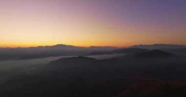 Hava manzarası, sabah güneşinin sisli denizin üzerindeki altın ışığı. Vadide sakin bir akşam atmosferi oluşur. Dağ sırasının renkli renkleri.