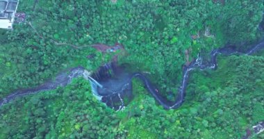Görkemli bir şelalenin, yemyeşil bir uçurumdan, sisli bir havuza dökülüşünün havadan görüntüsü. Canlı yeşillik ve dramatik düşüş çarpıcı bir doğal manzara yaratır.