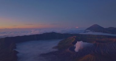 Şafak vakti gizlenmiş volkanik tepelerin hayranlık uyandırıcı hava manzarası engebeli araziyi ve manzaranın sakin atmosferini yakalıyor. Narin sabah ışığı dokuları güçlendirir.