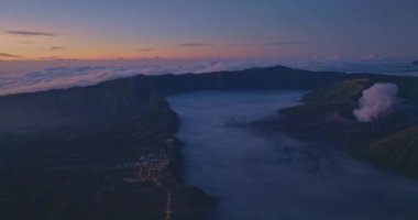 Şafak vakti gizlenmiş volkanik tepelerin hayranlık uyandırıcı hava manzarası engebeli araziyi ve manzaranın sakin atmosferini yakalıyor. Narin sabah ışığı dokuları güçlendirir.