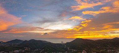 Phuket tepelerinin üzerinde canlı bir günbatımının nefes kesici hava manzarası. Tepenin tepesindeki Phuket Büyük Buda. Gökyüzü, günün son ışığı olarak koyu portakallar, kırmızılar ve morlarla boyanır.