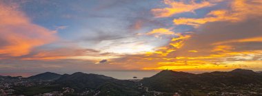 Phuket tepelerinin üzerinde canlı bir günbatımının nefes kesici hava manzarası. Tepenin tepesindeki Phuket Büyük Buda. Gökyüzü, günün son ışığı olarak koyu portakallar, kırmızılar ve morlarla boyanır.