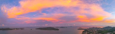 Phuket tepelerinin üzerinde canlı bir günbatımının nefes kesici hava manzarası. Tepenin tepesindeki Phuket Büyük Buda. Gökyüzü, günün son ışığı olarak koyu portakallar, kırmızılar ve morlarla boyanır.
