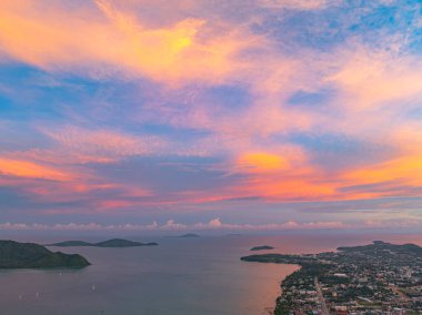 Gün batımında yumuşak pastel renklerle yıkanan Phuket adalarının hava manzarası. Aşağıdaki sakin deniz adalarla dolu, yukarıdaki gökyüzü ise narin pembe ve turuncu bulutlarla boyanmış..