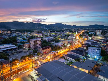 Alacakaranlıktaki Phuket şehrinin büyüleyici hava manzarası sokakları aydınlatan canlı şehir ışıklarıyla. Gökyüzünün yumuşak renkleri uzak ufukla kusursuz bir şekilde harmanlanarak, dinginlik yaratır.