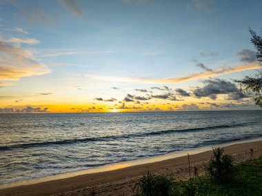 Sahil şeridinde dalgalanan yumuşak okyanus dalgalarıyla canlı gün batımı gökyüzü