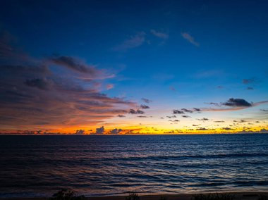 Sahil şeridinde dalgalanan yumuşak okyanus dalgalarıyla canlı gün batımı gökyüzü
