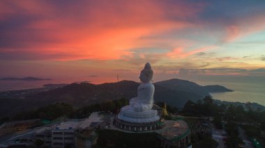 Canlı bir gün batımına bakan görkemli Büyük Buda heykelinin nefes kesici manzarası. Gökyüzü pembe, turuncu ve mor renklerle boyanarak dağların tepesinde ruhani bir atmosfer yaratıyor..