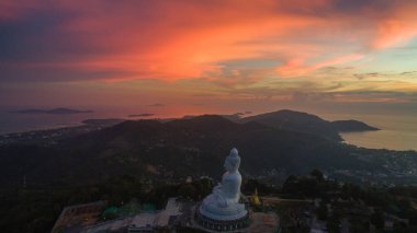 Canlı bir gün batımına bakan görkemli Büyük Buda heykelinin nefes kesici manzarası. Gökyüzü pembe, turuncu ve mor renklerle boyanarak dağların tepesinde ruhani bir atmosfer yaratıyor..
