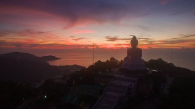 Canlı bir gün batımına bakan görkemli Büyük Buda heykelinin nefes kesici manzarası. Gökyüzü pembe, turuncu ve mor renklerle boyanarak dağların tepesinde ruhani bir atmosfer yaratıyor..